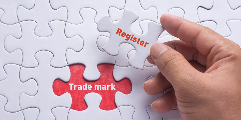 Puzzle piece that says trade mark and a hand holding a puzzle piece that says register