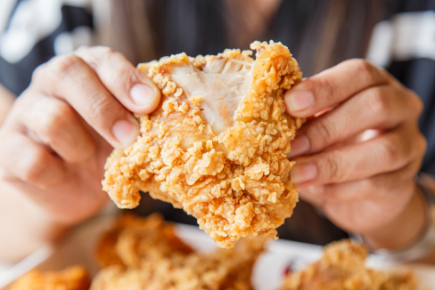 Hands delicately tearing a piece of fried chicken in half. 